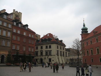 People walking on street amidst buildings in town against sky