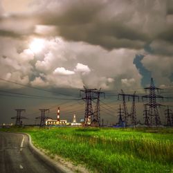 Electricity pylon on field against cloudy sky