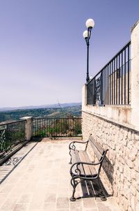 Empty bench by street against sky