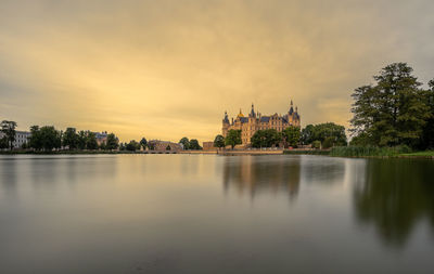Scenic view of lake by buildings against sky during sunset