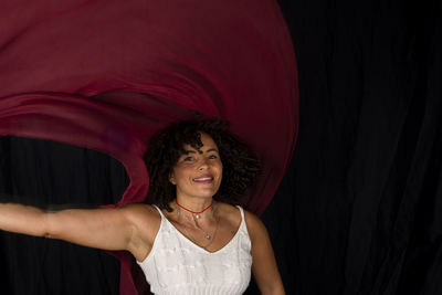 Woman moving a red cloth over her head against a black background. happy woman. salvador, brazil.