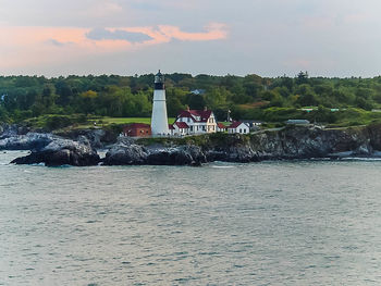 View of lighthouse in front of calm sea against cloudy sky