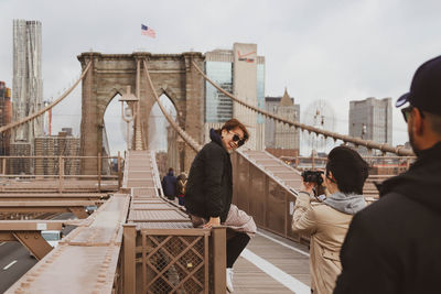 People on bridge against sky in city