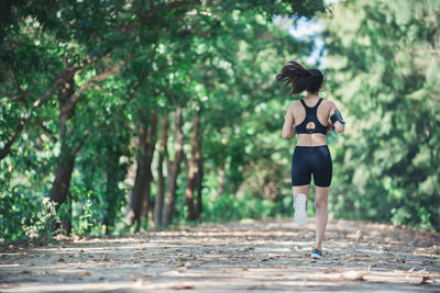 Full length rear view of young woman jogging on road amidst trees