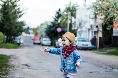 Cute girl pointing and looking away while standing on road