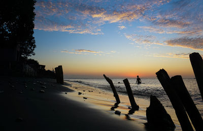 Silhouette wooden posts on beach against sky during sunset