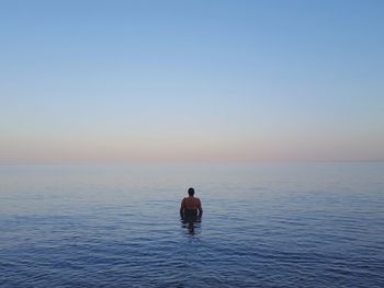 Rear view of man swimming in sea against clear sky