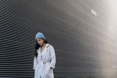 Woman standing with hands in pockets at black wall