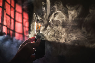 Close-up of cropped hand holding electronic cigarette by smoke at home