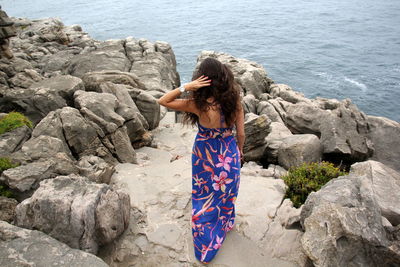 Rear view of woman standing on rock at sea shore