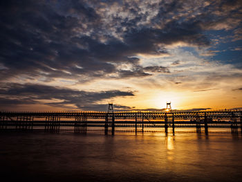 Silhouette bridge over sea against sky during sunset