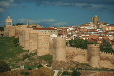 Stone towers with large wall over the hill, encircling the avila houses at sunset, in spain.