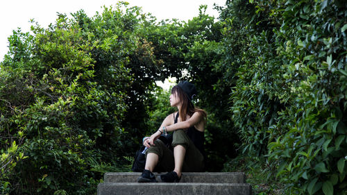 Woman sitting on staircase against plants at park