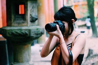 Woman holding camera while standing outdoors