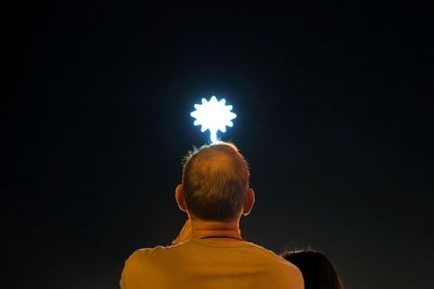 Rear view of man holding illuminated lighting equipment