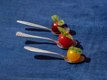 Cherry tomatoes with basil in spoons on a blue jeans background. minimal creative food concept.