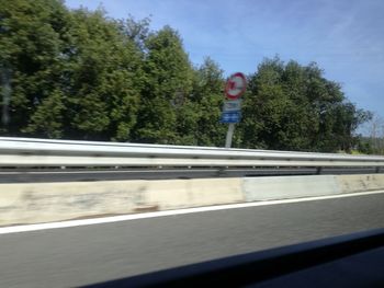 Road sign by trees against sky