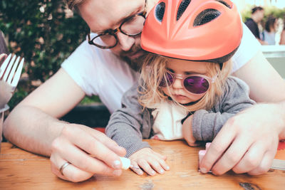 High angle view of father painting daughter fingernails on table outdoors