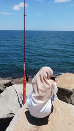 Rear view of woman photographing while crouching on rock at beach