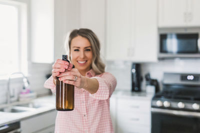 Portrait of smiling young woman spraying sanitizer at home