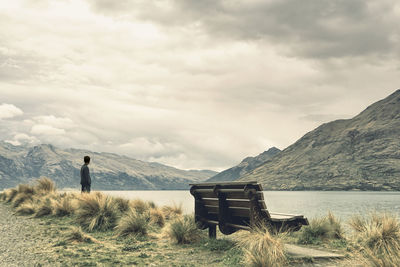 Man standing by lake against cloudy sky