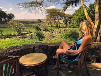 Side view of young woman sitting on chair by retaining wall at amboseli national park