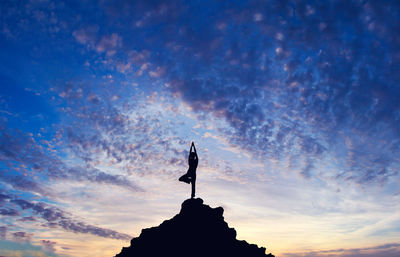 Silhouette of person doing yoga pose on mountain