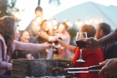 Cropped hand holding drinking glass while cooking food over grill