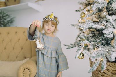 Cute girl holding decoration while standing by christmas tree