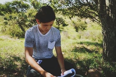 Teenage boy reading book while sitting on field