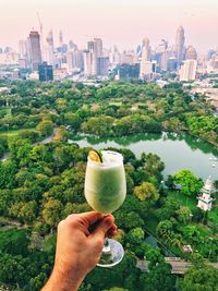 Midsection of man holding drink against buildings in city