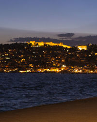 Illuminated city by sea against sky at night
