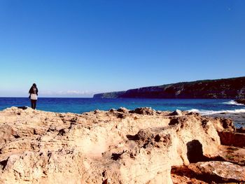 Rear view of man standing at beach against clear blue sky