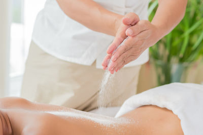 Midsection of therapist pouring talcum powder on woman back at health spa