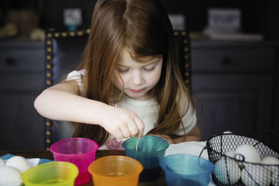 Cute girl coloring easter eggs on table at home