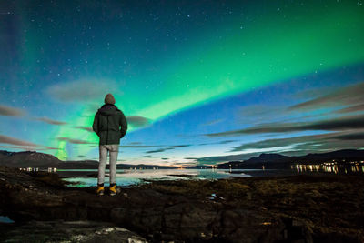 Rear view of man standing by sea against aurora borealis