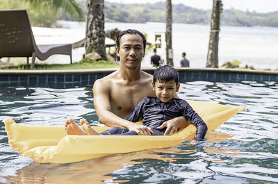 Portrait of shirtless father and son with inflatable in swimming pool