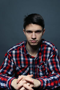 Portrait of young man sitting against gray background