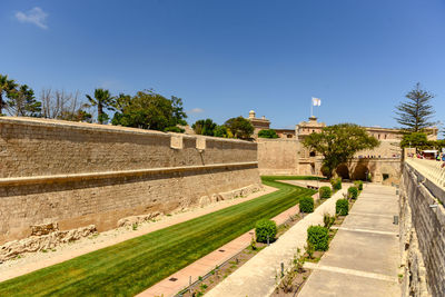 Footpath amidst buildings against clear blue sky