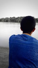 Rear view of man standing by lake against clear sky