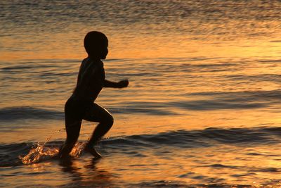 Full length boy running in sea during sunset