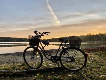 Bicycles on field by lake against sky during sunset