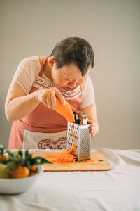 Lifestyle, education. an elderly woman with down syndrome rubs carrots on a grater, copy space