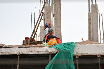 Woman sitting at construction site against sky