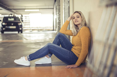 Full length portrait of young woman sitting in underground parking lot