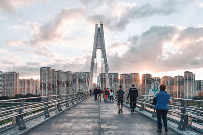 People walking on bridge against cloudy sky