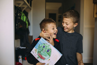 Cheerful boy holding brother's face while playing at home