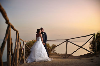 Bride and groom standing against sea during sunset