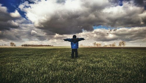 Man standing on grassy field against cloudy sky