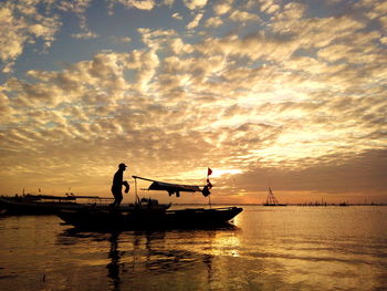 Silhouette man on boat against cloudy sky during sunset